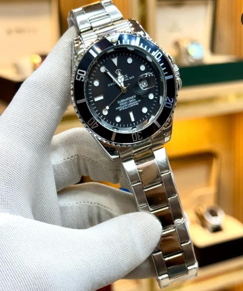 Silver watch with black dial held by a gloved hand against a blurred background